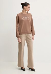 Felpa marrone con logo grafico, caratterizzata da un collo rotondo e maniche lunghe. Abbinata a pantaloni a gamba larga beige chiaro e tacchi neri.