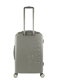 Maleta rígida gris con superficie texturizada, con detalles en relieve que dicen "NYC EST. 1989", ruedas dobles y asa extensible.