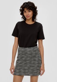 Zwarte katoenen T-shirt gecombineerd met een aansluitende mini-jurk in zwart-wit patroon, met textuurstof en intricatere horizontale lijnen.