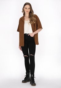 Hnědá semišová košile s krátkými rukávy, bílý top s krajkovým lemem, černé roztrhané skinny džíny a černé kotníkové boty s šněrováním a chunky podrážkou.