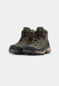 Brązowe i zielone buty trekkingowe z teksturowaną czarną gumową podeszwą, posiadające sznurowany fason oraz wyraźne logo z boku.