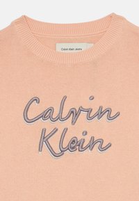 Persiko spalvos megztinis su pūkuota apykakle ir siuvinėtu „Calvin Klein“ logotipu pilka siūle.