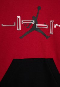 Silhouette nera di un giocatore di basket che salta con una palla, sovrapposta a del testo "JORDAN" frammentato in bianco e nero su un tessuto rosso e nero.