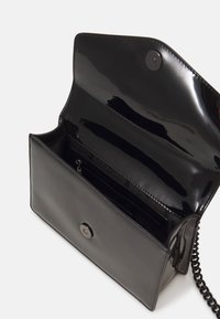 Czarna torebka z lakierowanej skóry z klapą, z zatrzaskiem i łańcuszkowym paskiem. Wnętrze zawiera kieszonkę na zamek oraz miejsca na karty.