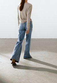 Beige ribbed sweater paired with light blue flared jeans. The jeans feature back pockets and a slight fade. Black and red sandals complete the look.