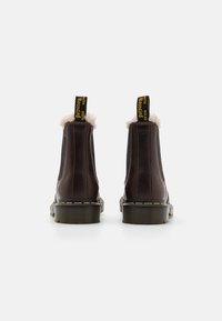 Stivaletti in pelle marrone con fodera in pelliccia sintetica, pannelli elasticizzati sui lati e cuciture gialle sulla suola. Presentano un anello per il tiraggio sul retro.