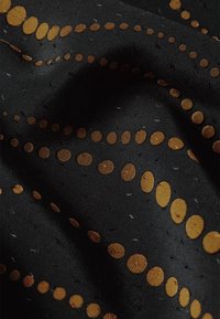 Tessuto nero con motivi circolari dorati di dimensioni variabili. Texture liscia con piccoli dettagli a punto in tutto il tessuto.