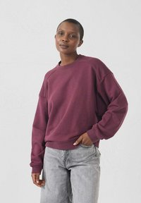Felpa bordeaux con collo rotondo e maniche raglan, realizzata in tessuto morbido. Abbinata a jeans grigi chiari con una vestibilità rilassata.