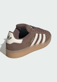 Brown suede sneaker with white leather accents, featuring three vertical stripes, textured finish, and a rubber sole. Logo on heel.