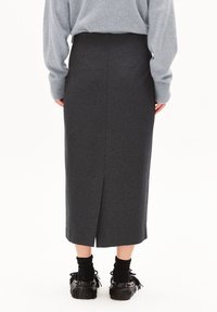 Middellange donkergrijze rok van zacht materiaal, met een split aan de achterkant. Gecombineerd met zwarte fringeschoenen en een textuurgrijze trui.