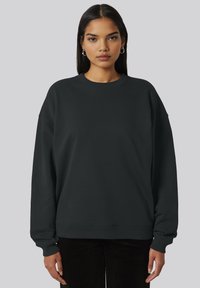 Felpa nera oversize con scollo rotondo, polsini e orlo a coste, realizzata con una texture morbida e liscia.