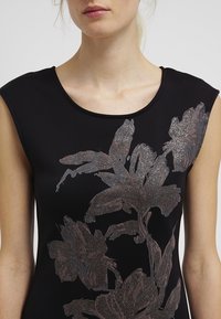 Haut noir sans manches avec un motif floral métallique en tons argentés et gris, près du corps avec un col rond et une texture lisse.