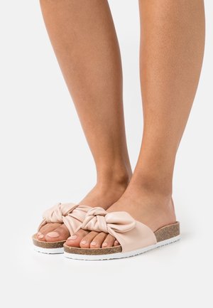 Sandalias deslizantes de cuero rosa con nudo frontal, suela texturizada, entresuela de corcho y base de goma blanca, que muestran un diseño casual y abierto en la punta.