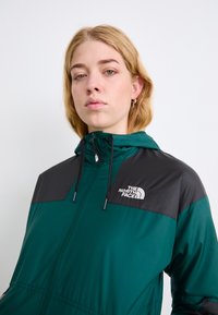 Roheline ja must kapuutsiga jakk esifermuuri tõmbega, millel on vasakul rinnal logo, valmistatud kergest, tekstureeritud kangast.