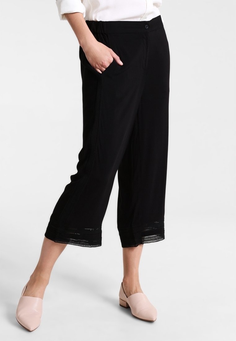 Svarta korta byxor med avslappnad passform, med sidofickor och spetsdetalj vid fållen. Materialet verkar lätt och mjukt.