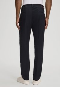 Pantalons noirs à taille élastique avec deux poches arrière, jambes droites et lignes épurées, associés à des baskets blanches. Texture de tissu lisse.