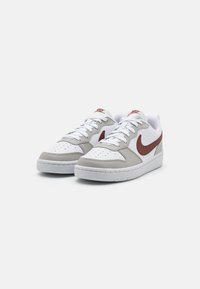 Witte en grijze sneaker met een rode Nike swoosh, bovenwerk van glad leer, geperforeerde neus, gewatteerde kraag en witte rubberen zool.