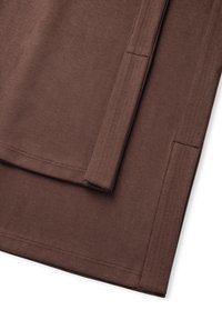 Bruine stof met een soepele textuur, met een detail van een naad en een gevouwen rand. Het materiaal lijkt zacht en lichtgewicht.