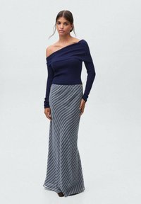 Mørkeblå off-shoulder ribbet bluse parret med en lang, mønstret nederdel med hundetanddesign i nuancer af blå og hvid.