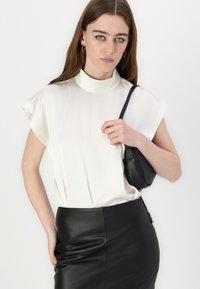 Blouse blanche à manches courtes avec un col montant ; associée à une jupe en cuir noir ajustée ; sac à main à la main ; texture lisse, design minimal.