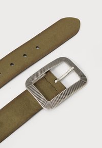 Cintura in suede verde oliva con una fibbia rettangolare decorativa in tonalità argento, caratterizzata da un bordo testurizzato e multiple fori di regolazione.
