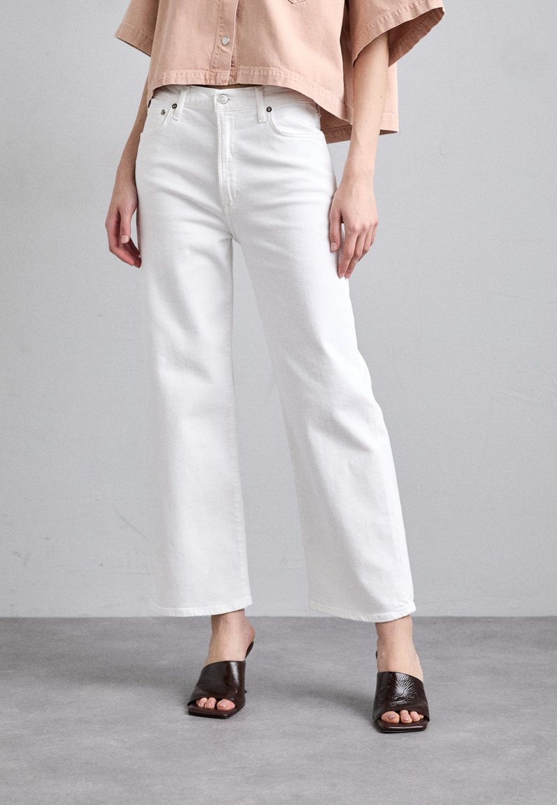 Witte wijde jeans met een hoge taille, gemaakt van denim, gecombineerd met donkerbruine open teen mules met een textuurafwerking.