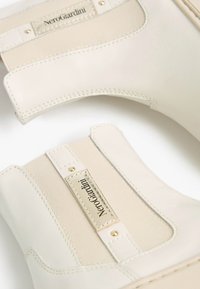 Beige Knöchelstiefel aus glattem Leder mit elastischen Einsätzen, goldenen Akzenten und "NeroGiardini"-Markierung auf einem genähten Etikett.