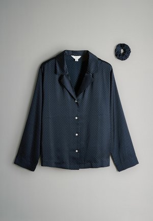 Tumši zilas pogāmo krekls ar baltiem punktiņiem, satīna tekstūra, garām piedurknēm un iegriezta apkakle, kopā ar saskaņotu scrunchie.