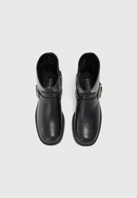 Bottines en cuir noir avec une texture lisse, une fermeture éclair sur le côté et un détail de boucle décoratif. Bout rond et design minimaliste.
