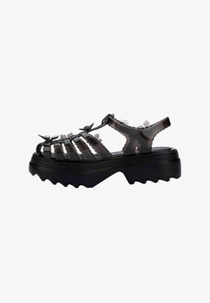 Sandalias de plataforma negras y gruesas con diseño recortado, correa ajustable y suela texturizada. Hechas de material brillante con detalles florales.