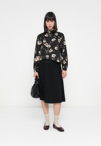 Svart blomstret bluse med lange ermer og hvite og gull blomster, sammen med et svart midikjørt. Tilbehøret inkluderer en svart veske og burgunder leiligheter.