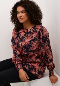Blouse à manches longues à motifs floraux avec des teintes de bleu marine et de rose. Présente un col rond et des poignets froncés, fabriquée en tissu léger.