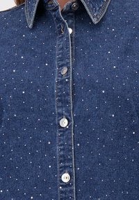 Camicia di denim con colletto classico, caratterizzata da un tessuto blu e da decorazioni di strass sparse sul petto e sul pattino dei bottoni.