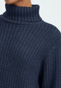 Marineblå strikket turtle neck sweater med et struktureret, ribbet mønster og en tyk krave. Stoffet ser blødt og varmt ud.