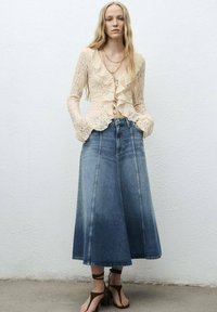Crème kanten cardigan met geschulpte randen, gecombineerd met een blauwe denim midi-jurk met stiksel.details. Bruine sleehakken maken de look compleet.