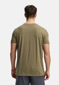 Camiseta de algodón verde oliva con cuello redondo y mangas cortas. Presenta una textura suave y un corte recto, se muestra desde la parte de atrás.