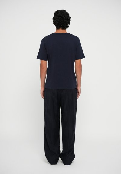 Camiseta de algodón azul marino de manga corta y cuello redondo, combinada con pantalones holgados a rayas negras, vista desde atrás.