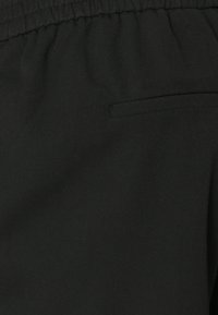 Svart stoff med en myk tekstur, med elastisk midjebånd og en liten, diskré sidelomme. Enkel og funksjonell design.