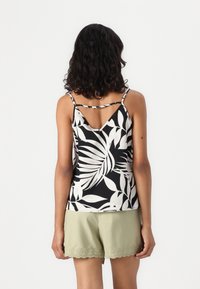 Haut sans manches noir et blanc avec un motif de feuilles, présentant un dos en V et des bretelles fines. Accompagné de shorts vert clair avec un bord festonné.