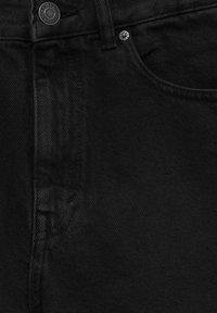 Détail d'un jean en denim noir montrant la poche avant, la passants de ceinture, les coutures et le bouton métal avec embossage de la marque.