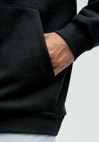 Zwarte katoenen hoodie met een voorzak en ribgebreide manchetten, met een zachte textuur en een relaxte pasvorm.