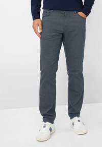 Donkergrauwe broeken met een visgraatpatroon, slim fit, voorzakken en een tailleband. Gecombineerd met witte sneakers met blauwe accenten.