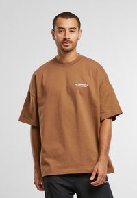 Brun oversized t-shirt i blødt stof med korte ærmer. Har hvid "RETERNITY" tekst på venstre bryst. Enkel, boksformet silhuet.