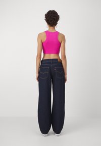 Fuksia crop tank top ja tummansiniset leveälahkeiset farkut. Farkuissa on takataskut, joissa on näkyvää tikkausta ja nahkalaatta vyötäröllä.