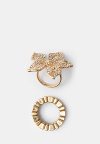 Set di gioielli in tonalità oro composto da un anello floreale abbellito con pietre trasparenti e un anello testurizzato con forme geometriche.
