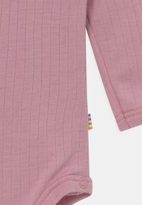 Rosa gerippter Baby-Body mit langen Ärmeln, ausgestattet mit Druckknopfverschlüssen am Boden und einem mehrfarbigen Etikett an der Seite.