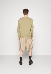 Khaki sweter z okrągłym dekoltem, w połączeniu z beżowymi szortami w paski. Szorty mają pionowe paski w kolorze czerwonym, granatowym i brązowym oraz boczną kieszeń.