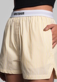 Yellow and white striped shorts in lightweight fabric, featuring an elastic waistband with "WRSTBVR" branding and side pockets.