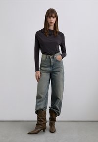 Long-sleeve, dark gray top paired with loose, light-washed high-waisted jeans and brown, slouchy ankle boots. Smooth textures and subtle details.