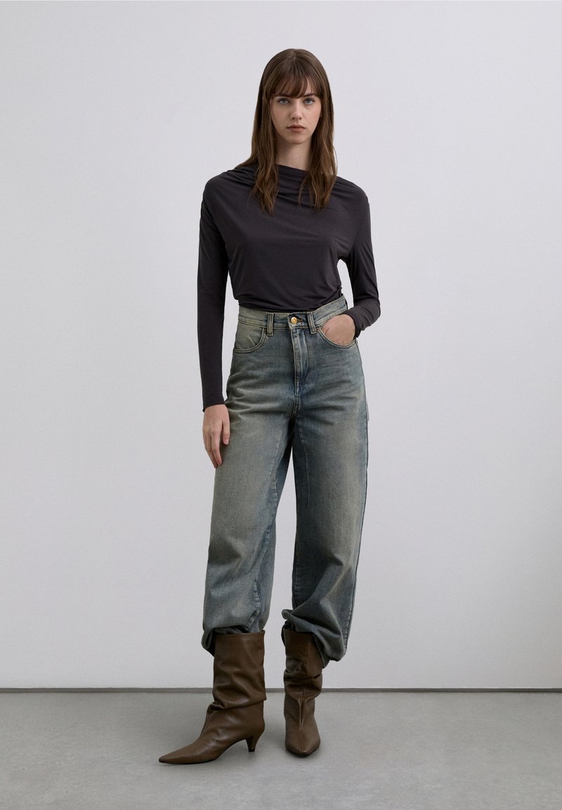Long-sleeve, dark gray top paired with loose, light-washed high-waisted jeans and brown, slouchy ankle boots. Smooth textures and subtle details.